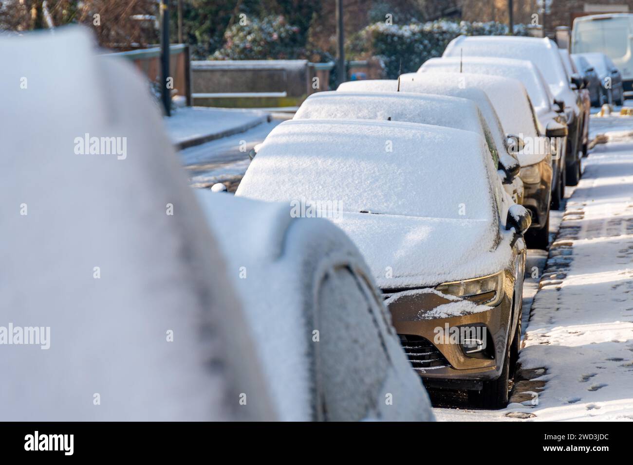 Fila di veicoli ricoperti da uno strato di neve parcheggiata per strada in una fredda e soleggiata mattinata invernale Foto Stock