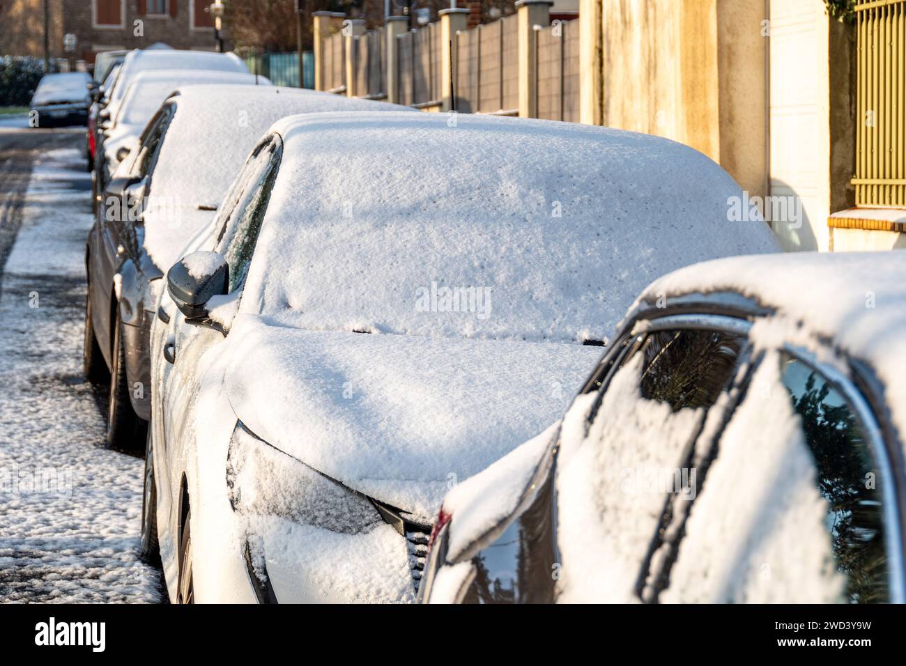 Fila di veicoli ricoperti da uno strato di neve parcheggiata per strada in una fredda e soleggiata mattinata invernale Foto Stock