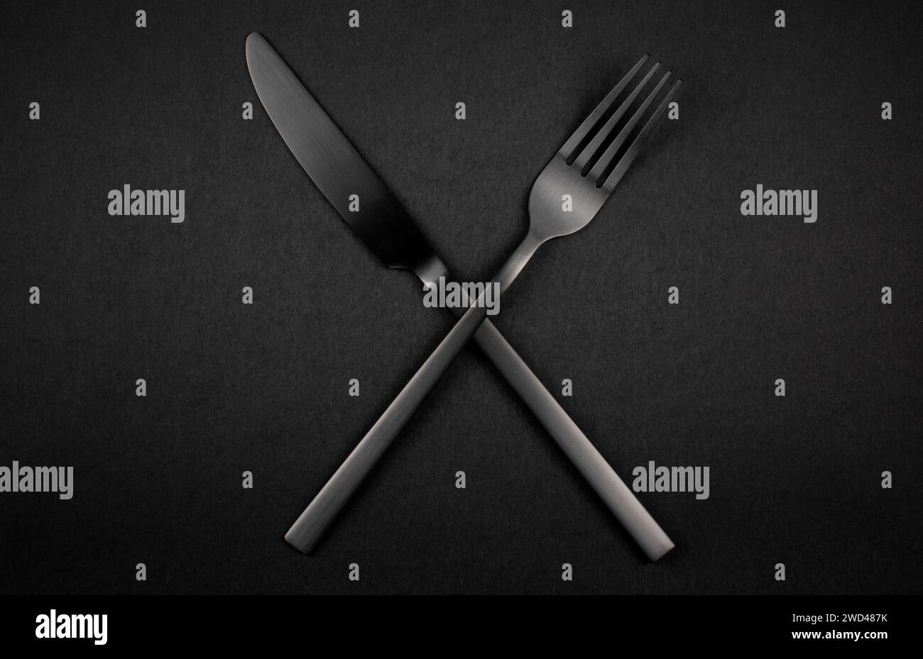 Forchetta e coltello incrociati neri su sfondo scuro. Set argenteria nera Foto Stock