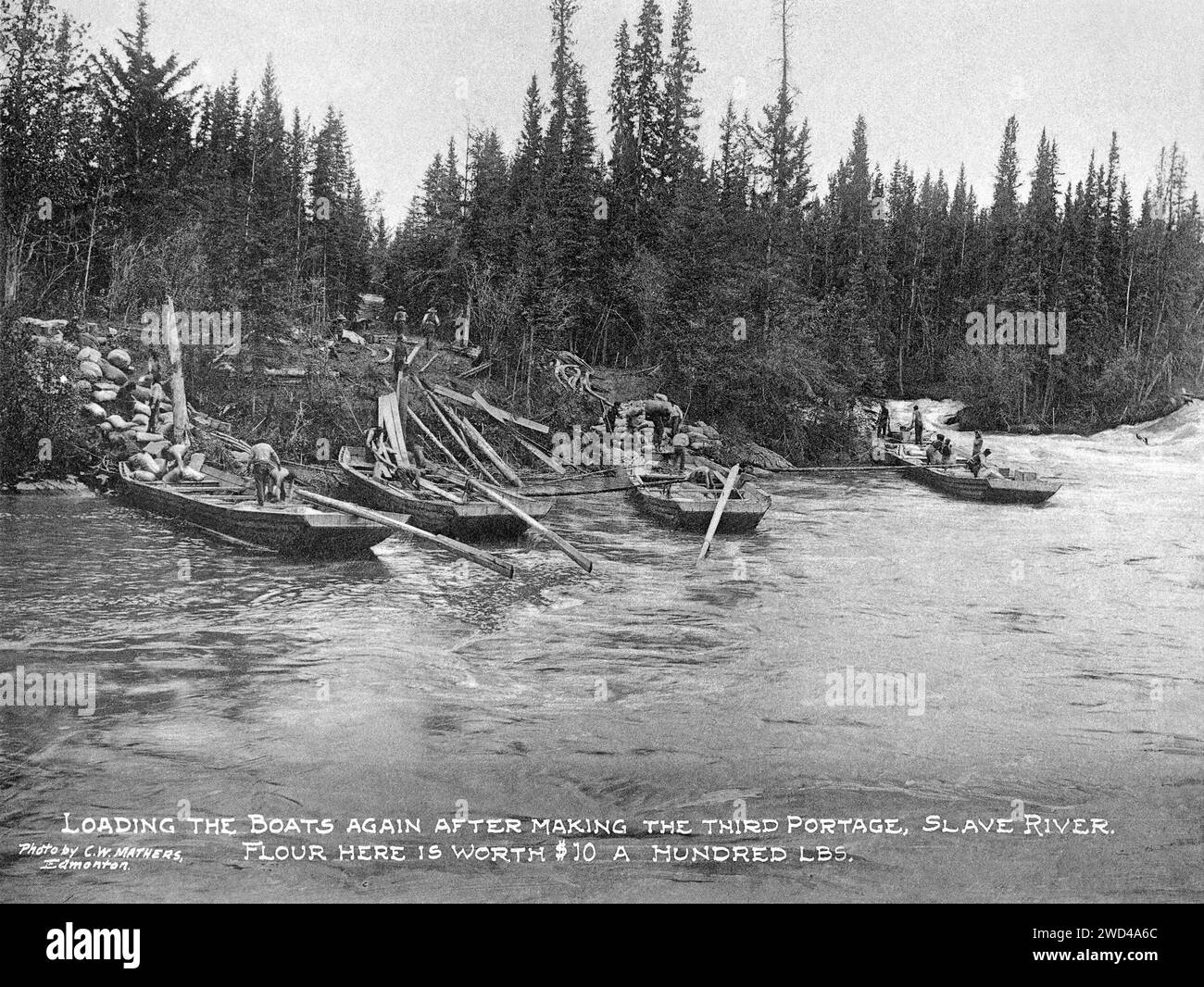 Una fotografia del 1901 di razzi da carico a fondo piatto, caricati dopo essere stati trasportati via terra in un porto sul fiume Slave in Alberta/territori del Nord-Ovest, scattata da C W Mathers in una spedizione nell'estremo nord del Canada e pubblicata nel suo libro «l'estremo Nord». Mathers didascalò questa foto: Caricare di nuovo le barche dopo aver fatto il terzo viaggio, Slave River. La farina qui vale 10 dollari a 100 libbre Foto Stock