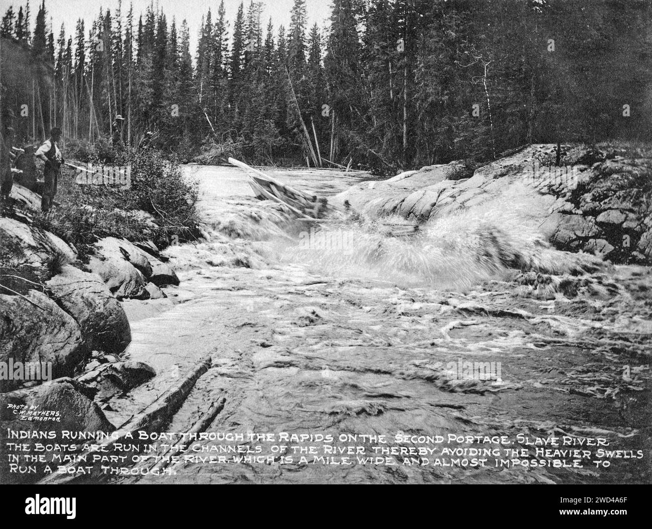 Una fotografia del 1901 di un cargo a fondo piatto che attraversa rapide su un canale laterale del fiume Slave in Alberta/territori del Nord-Ovest, scattata da C W Mathers in una spedizione nell'estremo nord del Canada e pubblicata nel suo libro «l'estremo Nord». Mathers ha descritto questa foto: Gli indiani [persone delle prime Nazioni] guidano una barca attraverso le rapide del secondo tratto, il fiume Slave. Le barche scorrono nei canali del fiume, evitando così i rigonfiamenti più pesanti nella parte principale del fiume, che è largo un miglio e quasi impossibile da attraversare. Foto Stock
