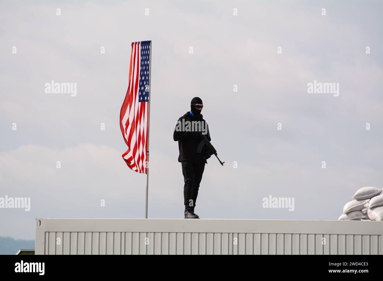 Criminale insorto con fucile d'assalto in piedi davanti alla bandiera americana. Foto Stock