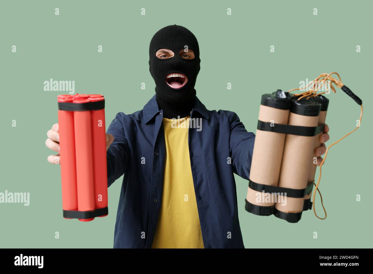 Bel giovane uomo felice in balaclava con bombe su sfondo verde Foto Stock