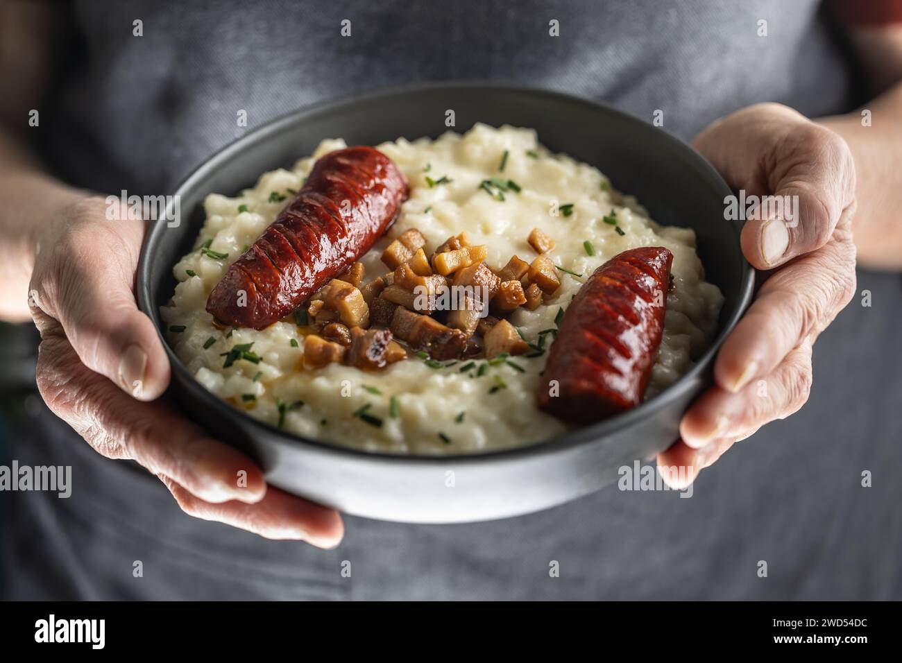 Le mani di un cuoco domestico senior tengono un piatto con un piatto nazionale slovacco - Bryndzove Halusky. Foto Stock