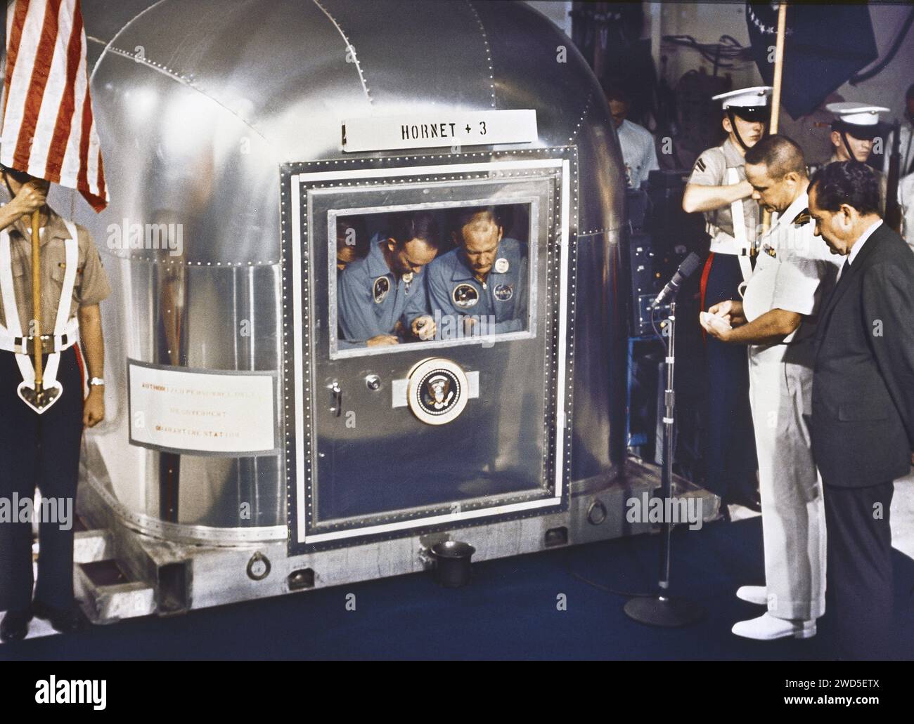 Gli astronauti dell'Apollo 11 Neil A. Armstrong, Edwin E. Aldrin e Michael Collins, all'interno della struttura di quarantena dopo la riuscita missione di recupero, come preghiera è offerta dal tenente comandante John Pirrto, USS Hornet Chaplain accompagnato dal presidente degli Stati Uniti Richard Nixon (fronte destro), USS Hornet, NASA, 24 luglio 1969 Foto Stock