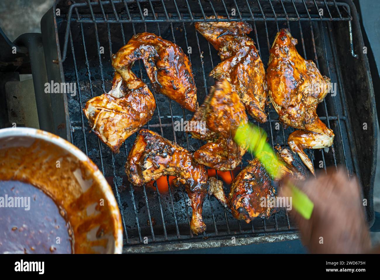 Zampa e coscia di pollo ricoperte di salsa barbecue e spezie, lo chef applica la salsa fatta in casa spazzolandola sulla carne Foto Stock