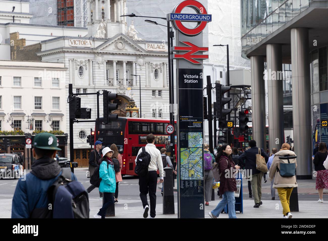 Segnaletica per le stazioni della metropolitana e ferroviaria di Victoria al livello della strada, con il Victoria Palace Theatre sullo sfondo e un autobus rosso di Londra Foto Stock