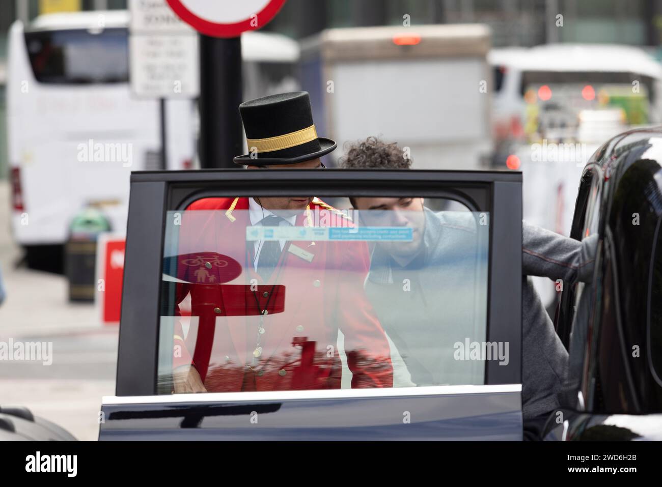 Un concierge vestito in elegante uniforme rossa tradizionale all'esterno del Rubens Hotel a Victoria, nel centro di Londra. Sta aiutando un passeggero a salire su un taxi nero Foto Stock