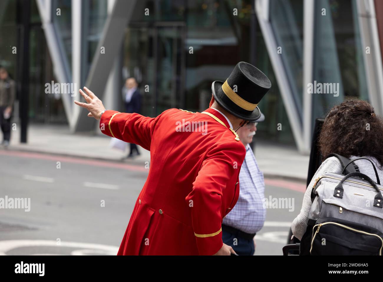 Un concierge vestito in elegante uniforme rossa tradizionale all'esterno del Rubens Hotel a Victoria, nel centro di Londra. Sta aiutando un passeggero a salire su un taxi nero Foto Stock