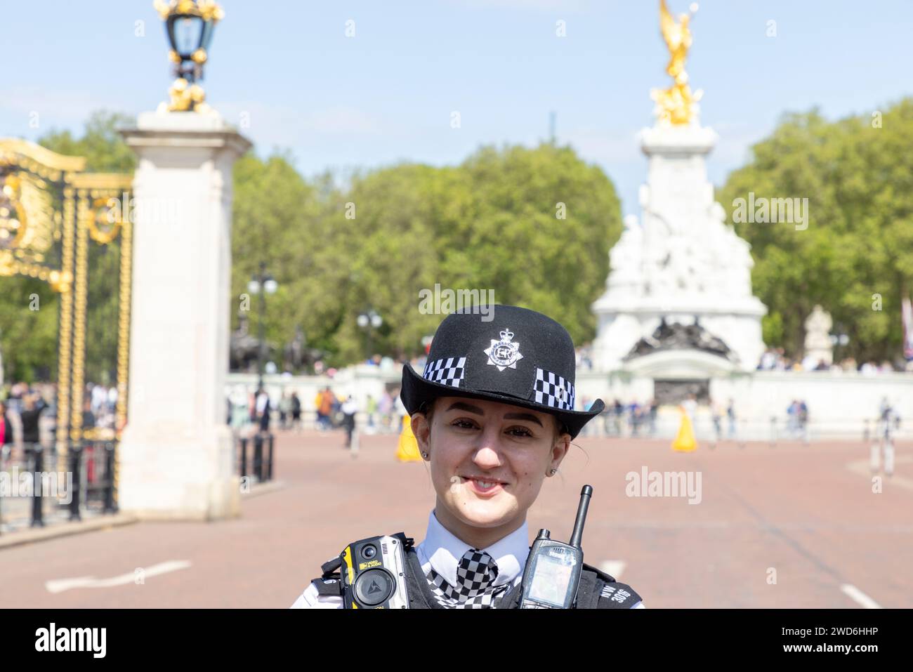 Una donna sorridente agente di polizia fuori Buckingham Palace, Londra. Dietro di lei si trova il Victoria Memorial. Foto Stock