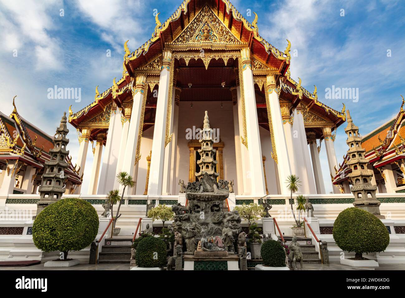 Ingresso al Tempio di Wat Suthat a Bangkok, thailandia. Giardino ornamentale di fronte. Altri edifici su entrambi i lati; cielo blu e nuvole sopra. Foto Stock