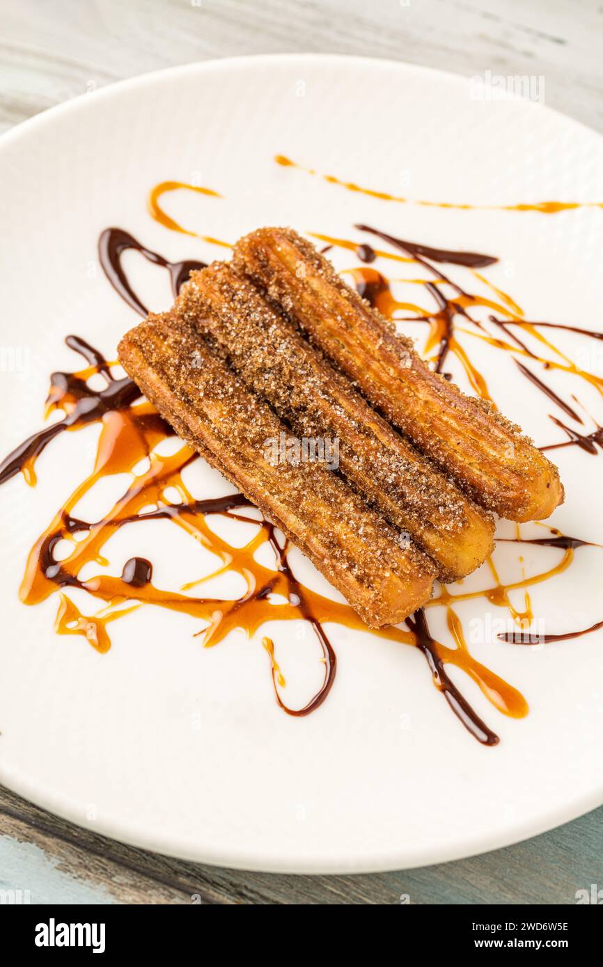 Churros caldi con salsa di cioccolato su tavola di legno. Foto Stock