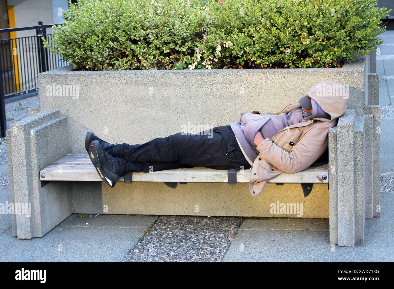 Un senzatetto che dorme sulla panchina nel centro di Vancouver, British Columbia, Canada Foto Stock