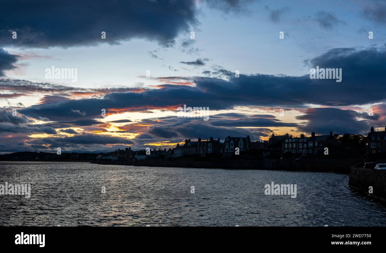 Una pittoresca scena costiera con incantevoli residenze sul mare che costeggiano la parete del mare al tramonto Foto Stock