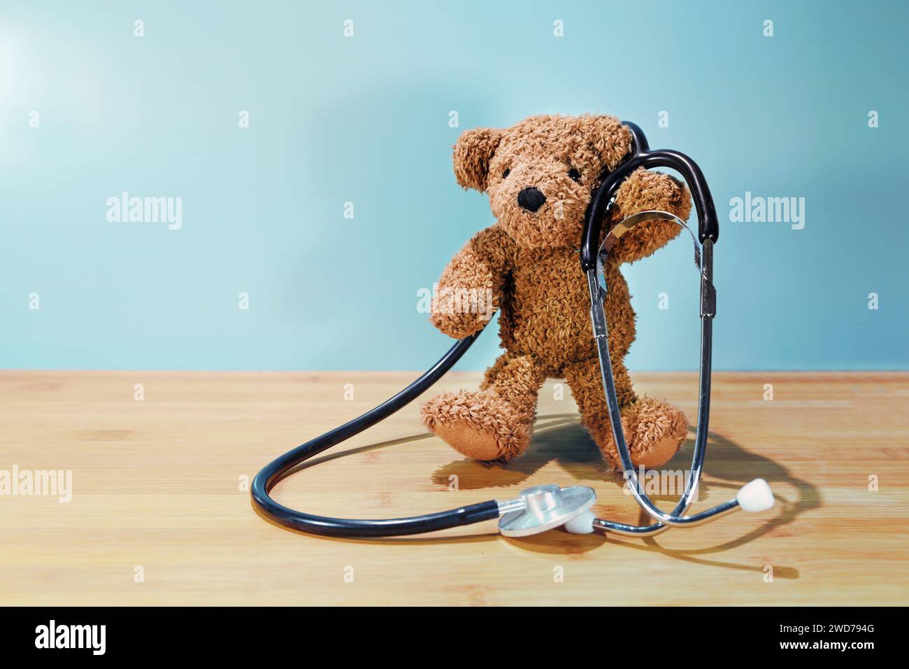 Orsacchiotto in piedi che regge uno stetoscopio su un tavolo di legno su uno sfondo turchese, concetto bambini per l'assistenza sanitaria, medico e pediatrico Foto Stock
