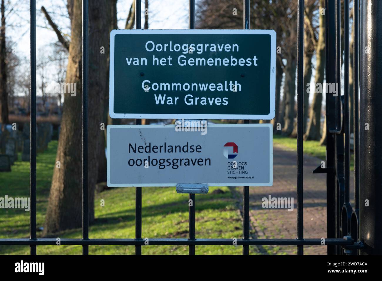 Insegna del Commonwealth War Graves Cemetery, con testo inglese e olandese. Dietro la recinzione le lapidi Foto Stock
