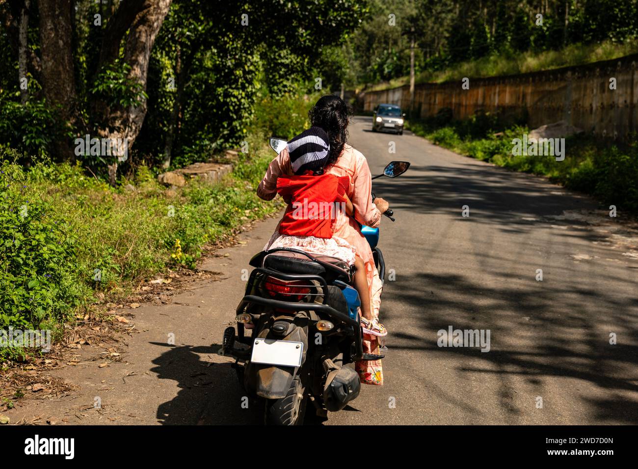 Una decisione di un secondo si svolge mentre una madre protegge istintivamente sua figlia su uno scooter Foto Stock