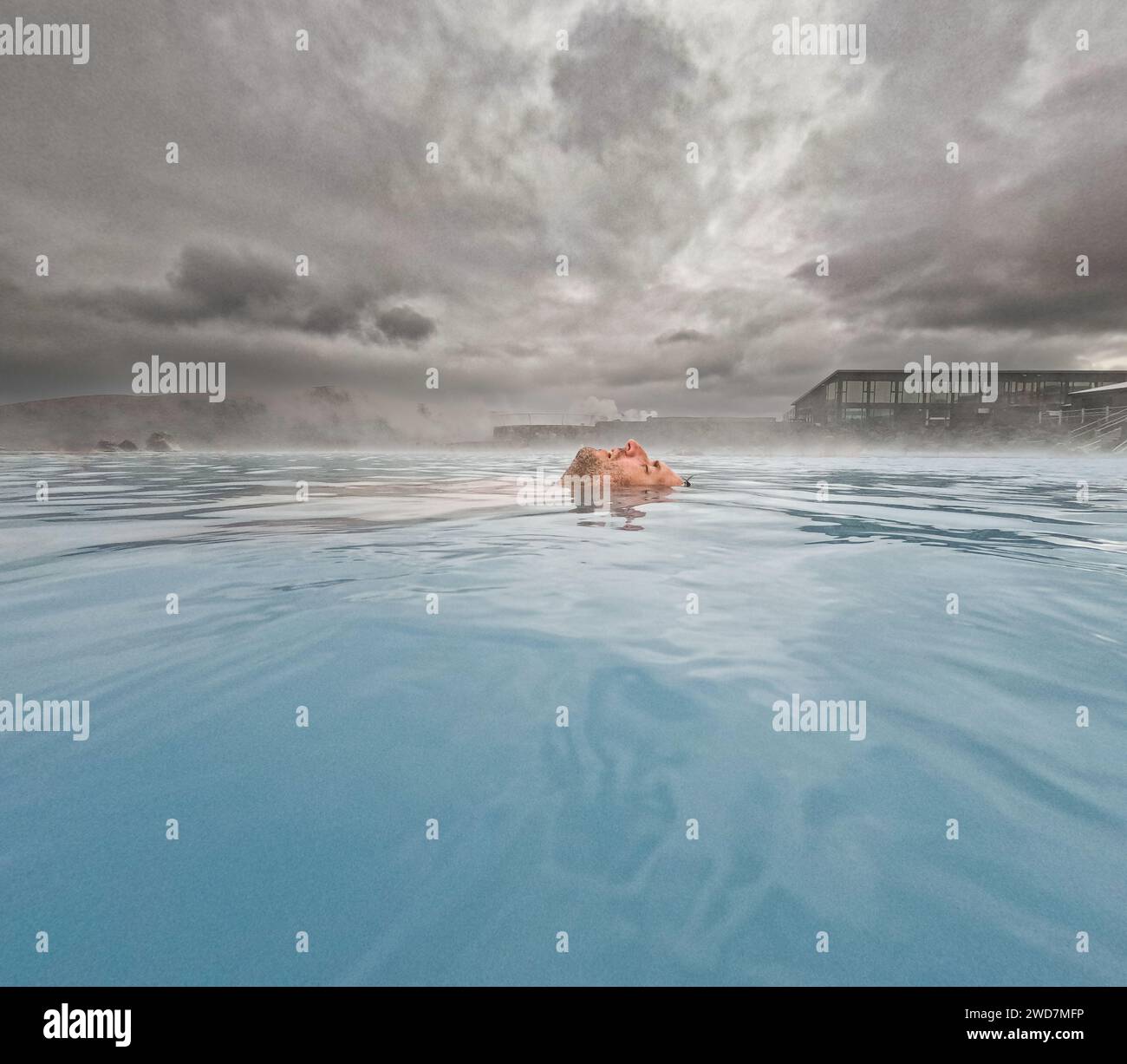 L'uomo galleggia nelle sorgenti termali blu con il vapore che fuoriesce dall'acqua Foto Stock