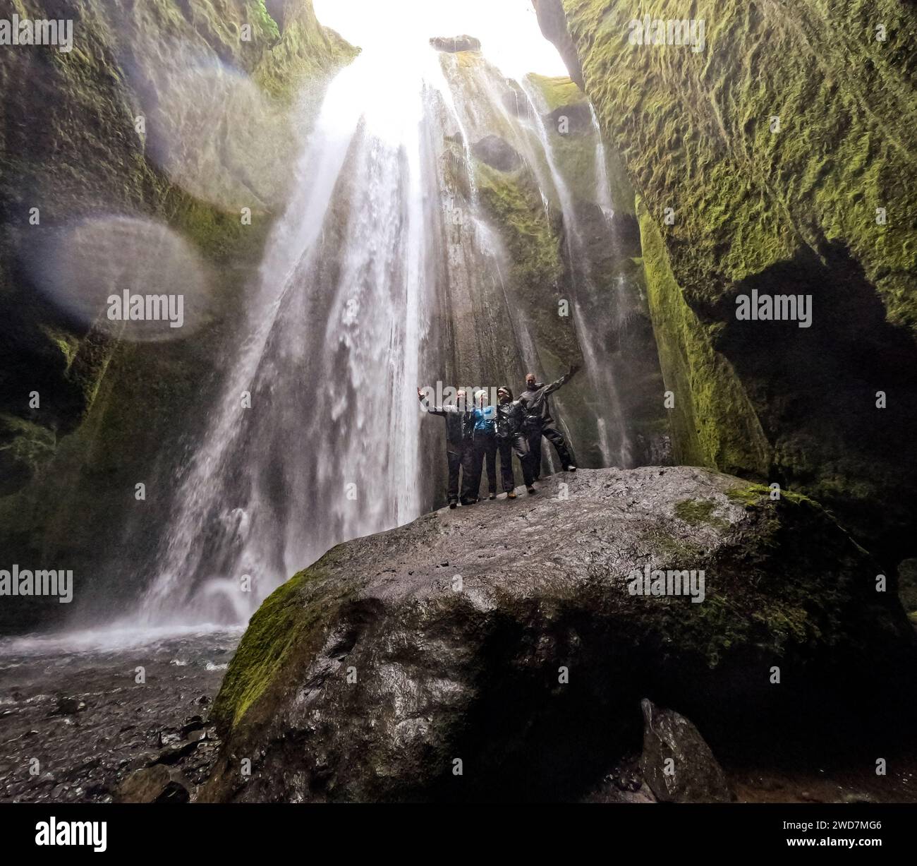 Gruppo di adulti su un'enorme roccia con una cascata che scende dalle scogliere Foto Stock