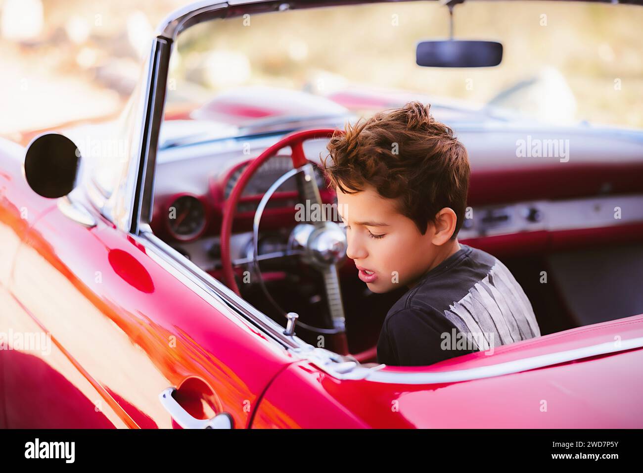 Giovane ragazzo seduto in un'auto classica rossa che finge di guidare Foto Stock