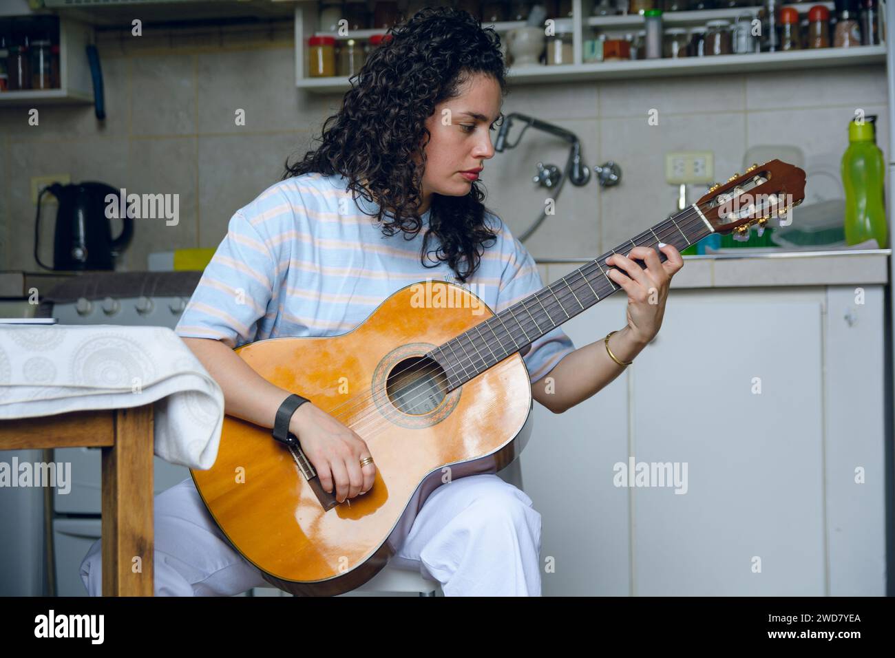 Vista frontale della giovane donna latina venezuelana, con i capelli ricci, studentessa di musica classica da sola a casa seduta concentrata sulla pratica su larga scala su acou Foto Stock