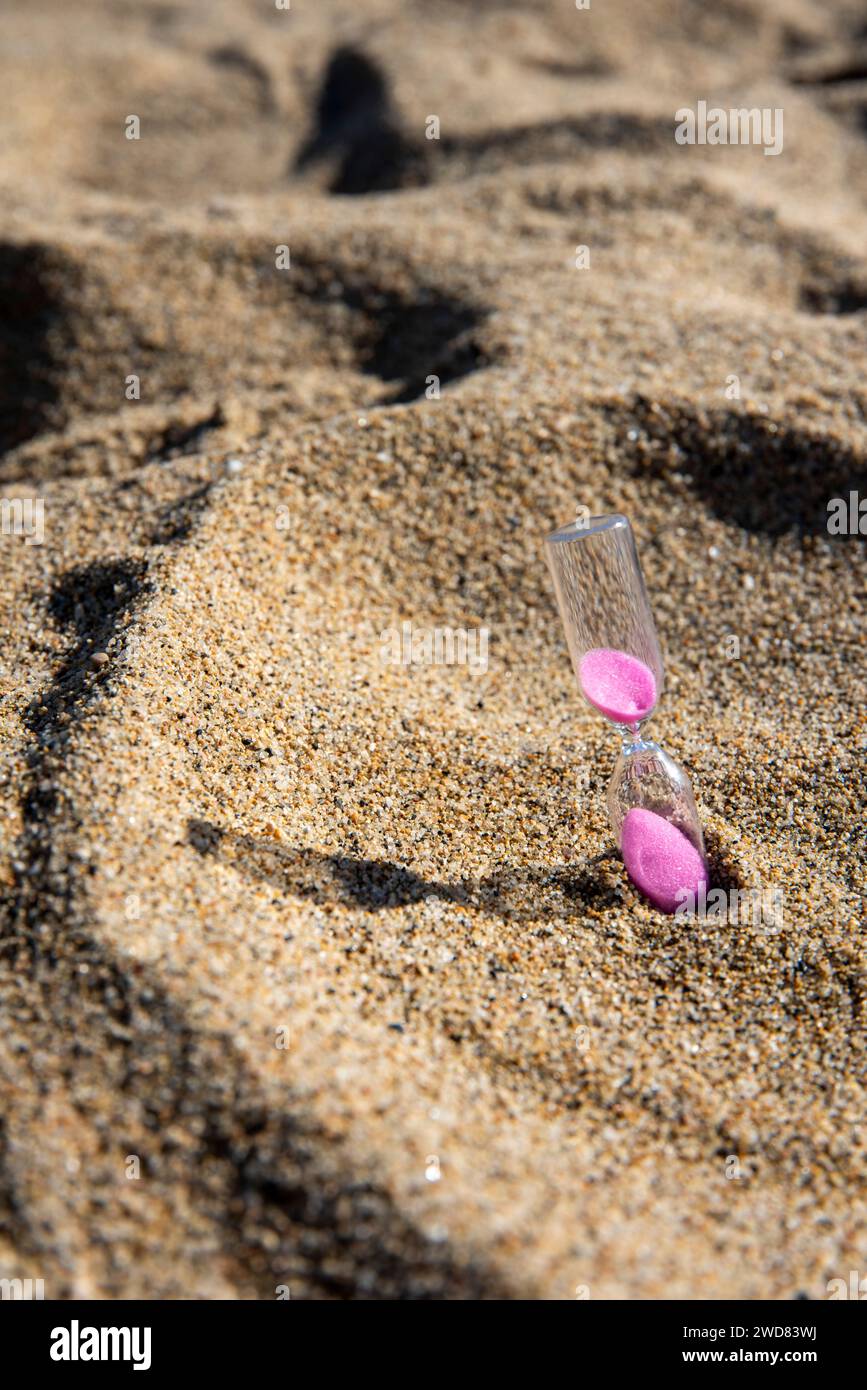 Le sabbie rosa scendono graziosamente in una clessidra sul mare, catturando momenti fugaci di tranquilla bellezza sulla spiaggia Foto Stock