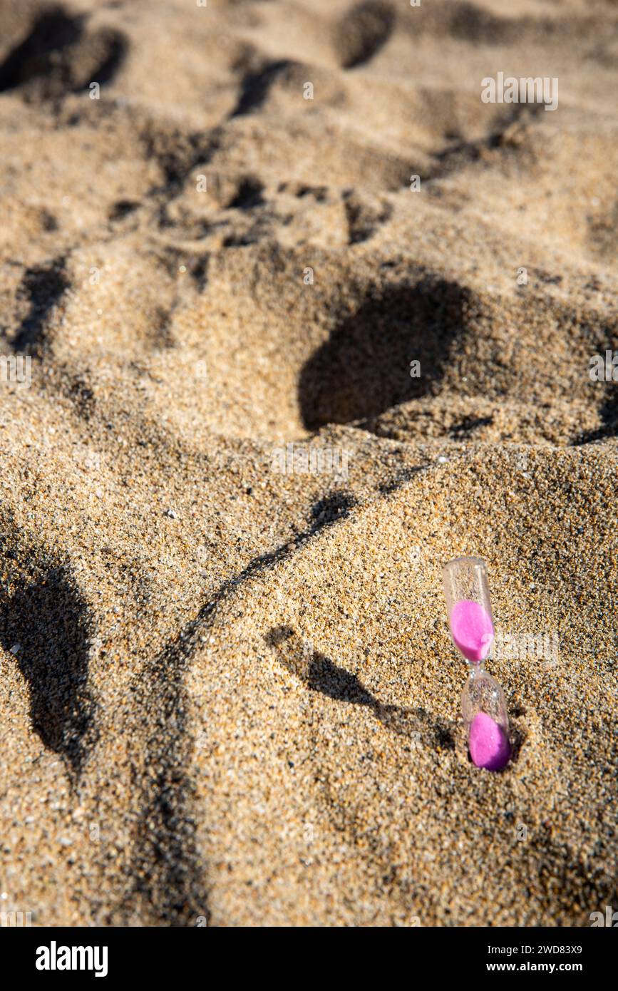 Le sabbie rosa scendono graziosamente in una clessidra sul mare, catturando momenti fugaci di tranquilla bellezza sulla spiaggia Foto Stock