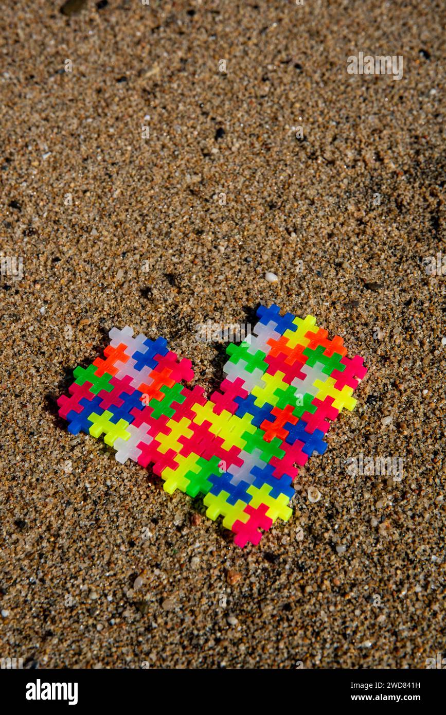 Puzzle Heart: Amore e connessione rappresentati da pezzi colorati di puzzle sulla spiaggia, a simboleggiare un legame unico e speciale Foto Stock