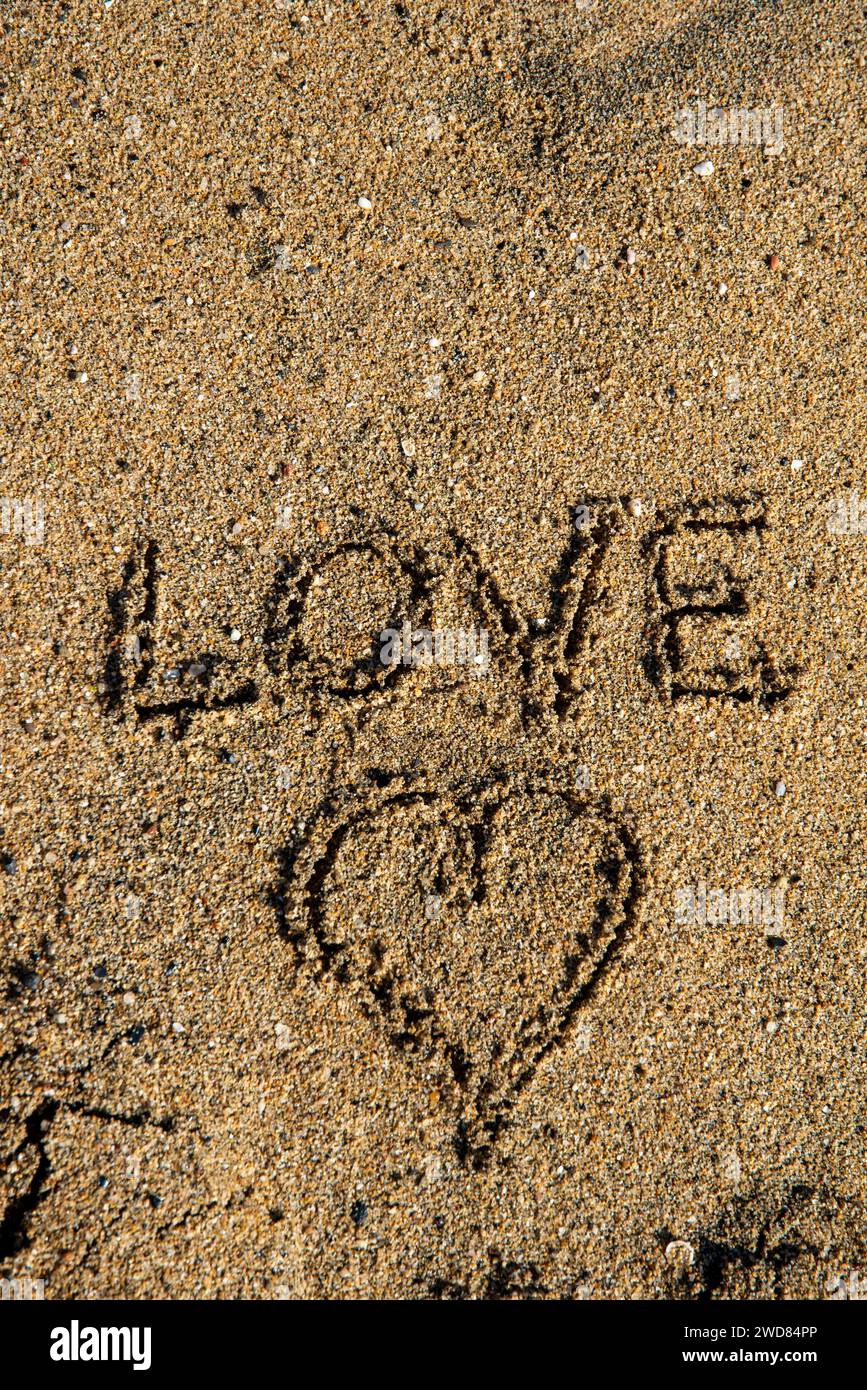 Lettera d'amore al mare: "Amore" e cuore disegnati nella sabbia, un romantico tableau impresso dalle onde Foto Stock