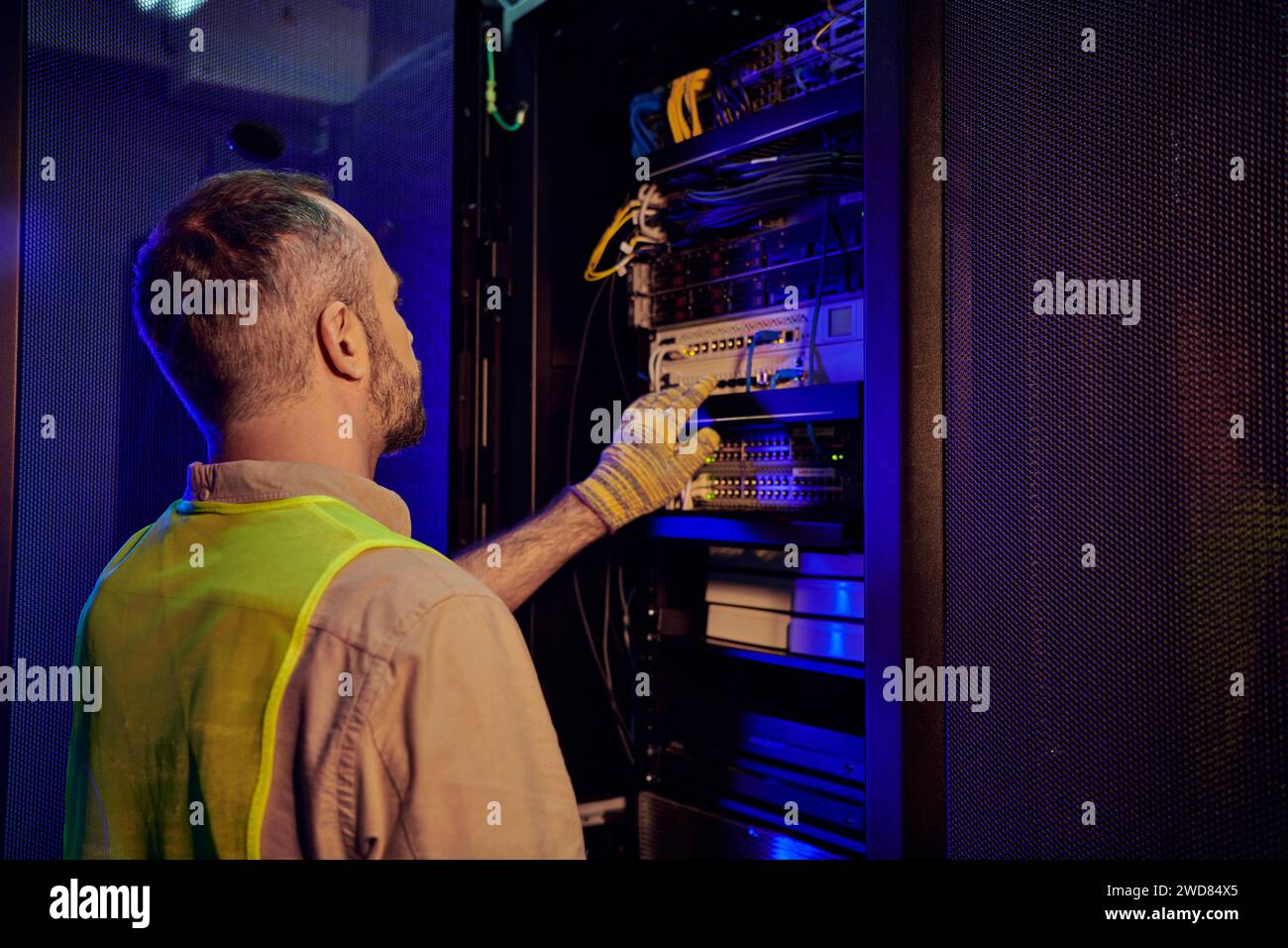 tecnico pensivo dedicato in abiti di sicurezza che ispeziona il centro informazioni e la memorizzazione dei dati Foto Stock