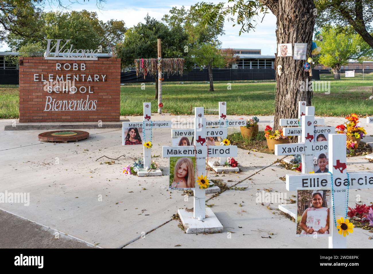 Monumento commemorativo con croci, cartello di benvenuto in mattoni per la Robb Elementary School, scuola con recinzione sullo sfondo, Uvalde, Texas, USA. Foto Stock