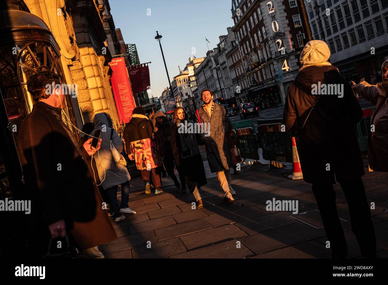 I pendolari si dirigono lungo Piccadilly in una serata d'inverno piena di sole mentre il sole basso tramonta a ovest verso Hyde Park, nel centro di Londra, nel Regno Unito Foto Stock