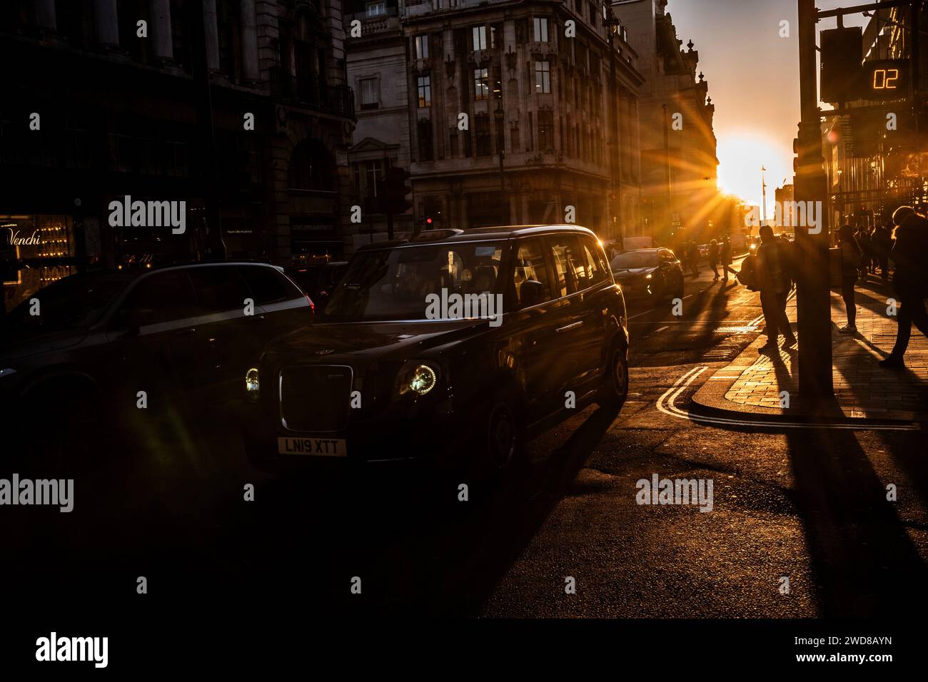 I pendolari si dirigono lungo Piccadilly in una serata d'inverno piena di sole mentre il sole basso tramonta a ovest verso Hyde Park, nel centro di Londra, nel Regno Unito Foto Stock