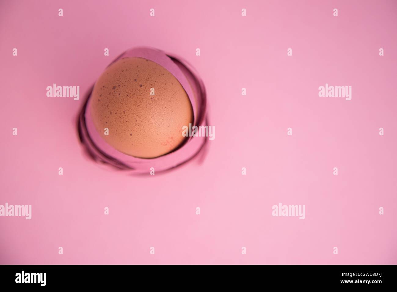 Buona Pasqua. Primo piano minimalista di un uovo avvolto in nastri colorati come se fosse un nido. Isolato su sfondo rosa. Foto Stock