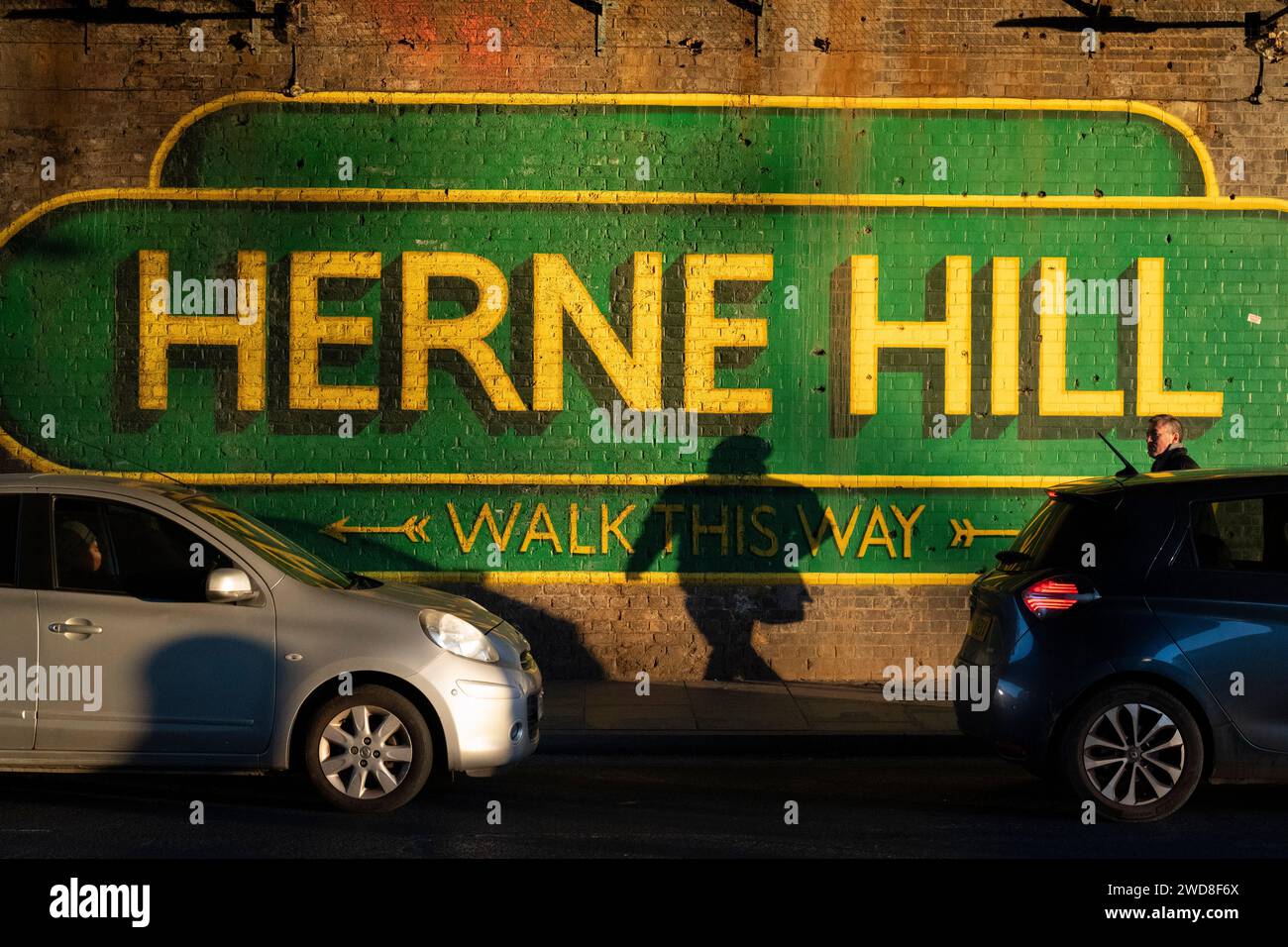 Un londinese e la sua ombra con la segnaletica sotto il ponte ferroviario a Herne Hill SE24, il 18 gennaio 2024, a Londra, in Inghilterra. Foto Stock
