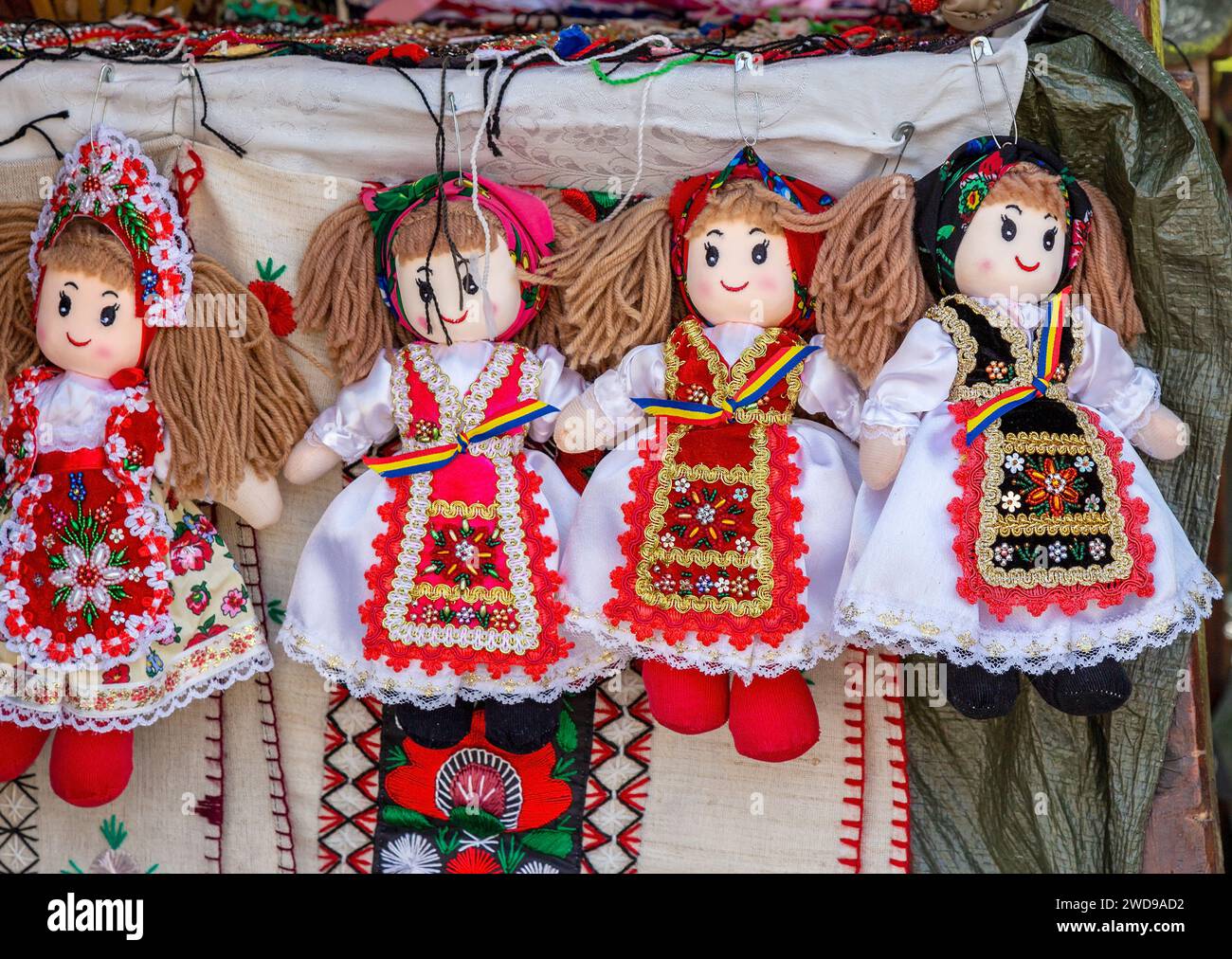 Bambole vestite con costumi tradizionali rumeni, adagiate su materiali ricamati ed esposte per la vendita. Foto Stock