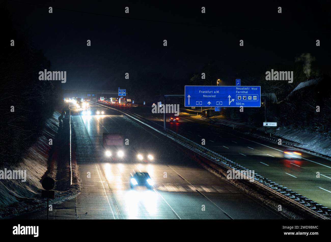 Traffico notturno sull'autostrada tedesca A3 tra le uscite di Bad Honnef e Neustadt con sfocatura del movimento e grandi segnali stradali durante le nevicate con grandi quantità di o Foto Stock