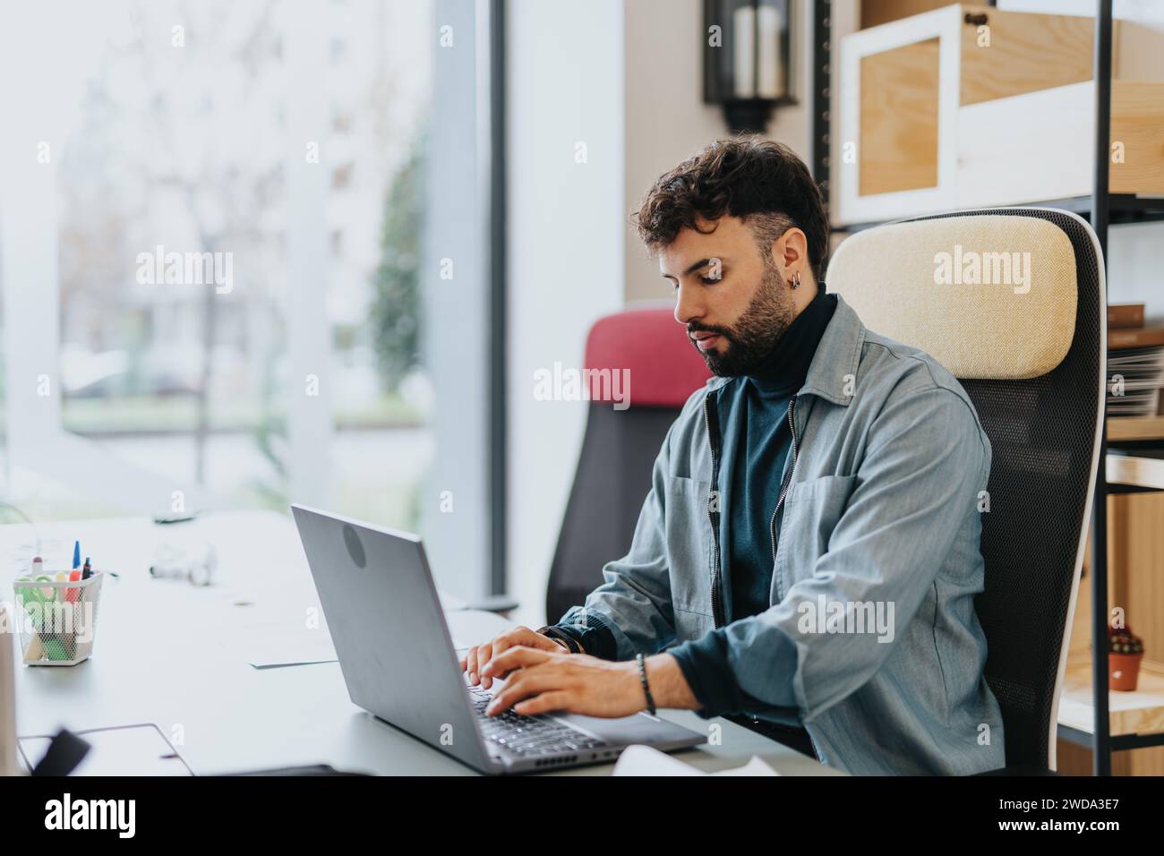 Un uomo nella moderna zona degli uffici, che si affida al suo portatile, affronta le attività con concentrazione e dinamismo tecnologico. Il lavoro è reale Foto Stock