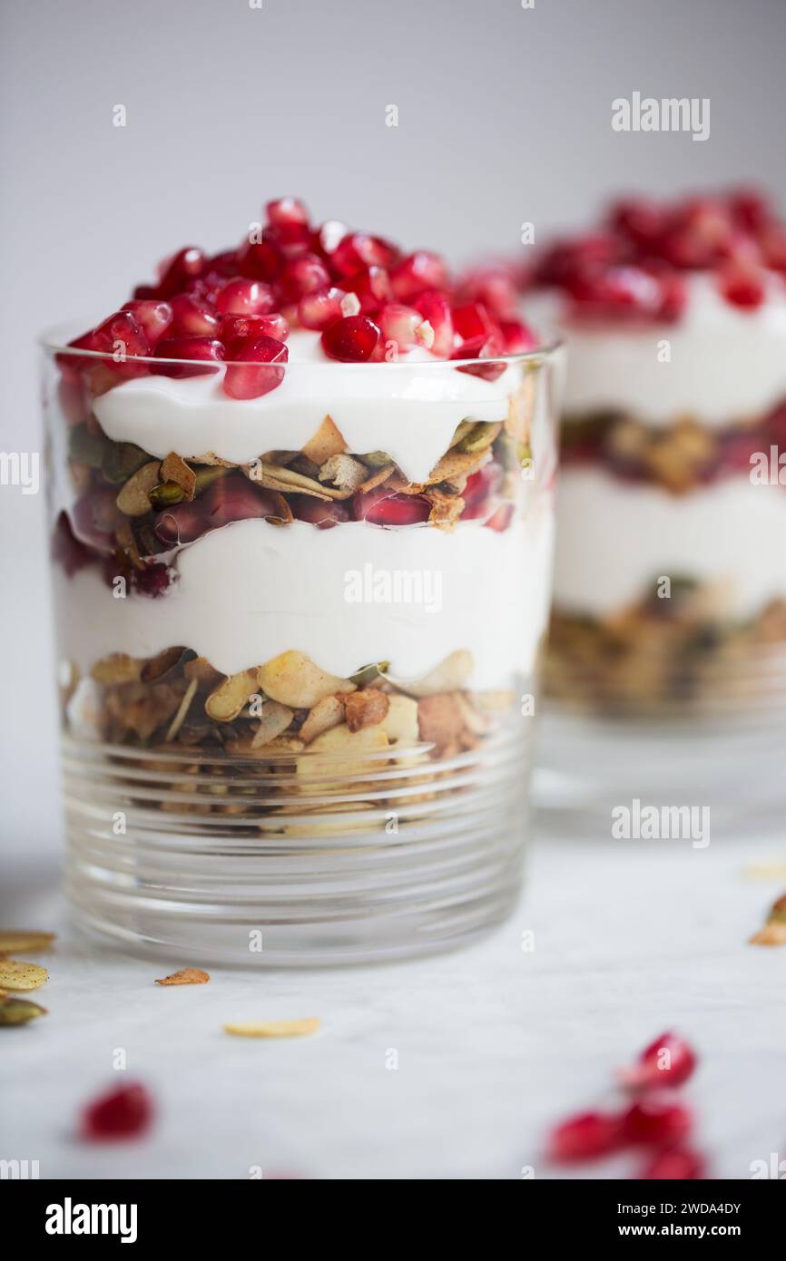 Parfait di yogurt a strati con muesli, semi e melograno fresco in vetro, sana colazione o idea di spuntino. Foto Stock