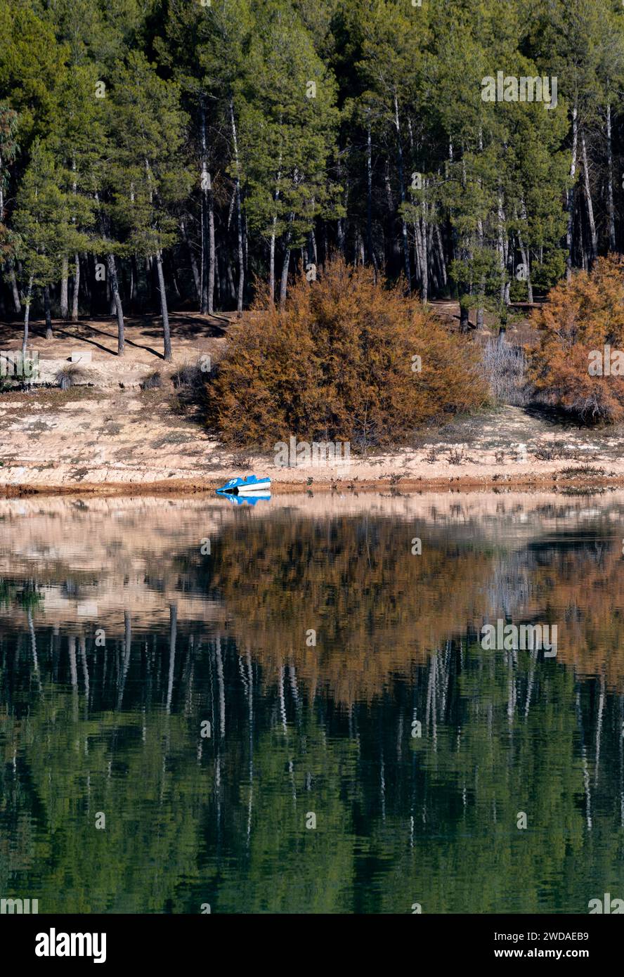 Riflessi della foresta e una barca blu nelle acque calme di un lago Foto Stock