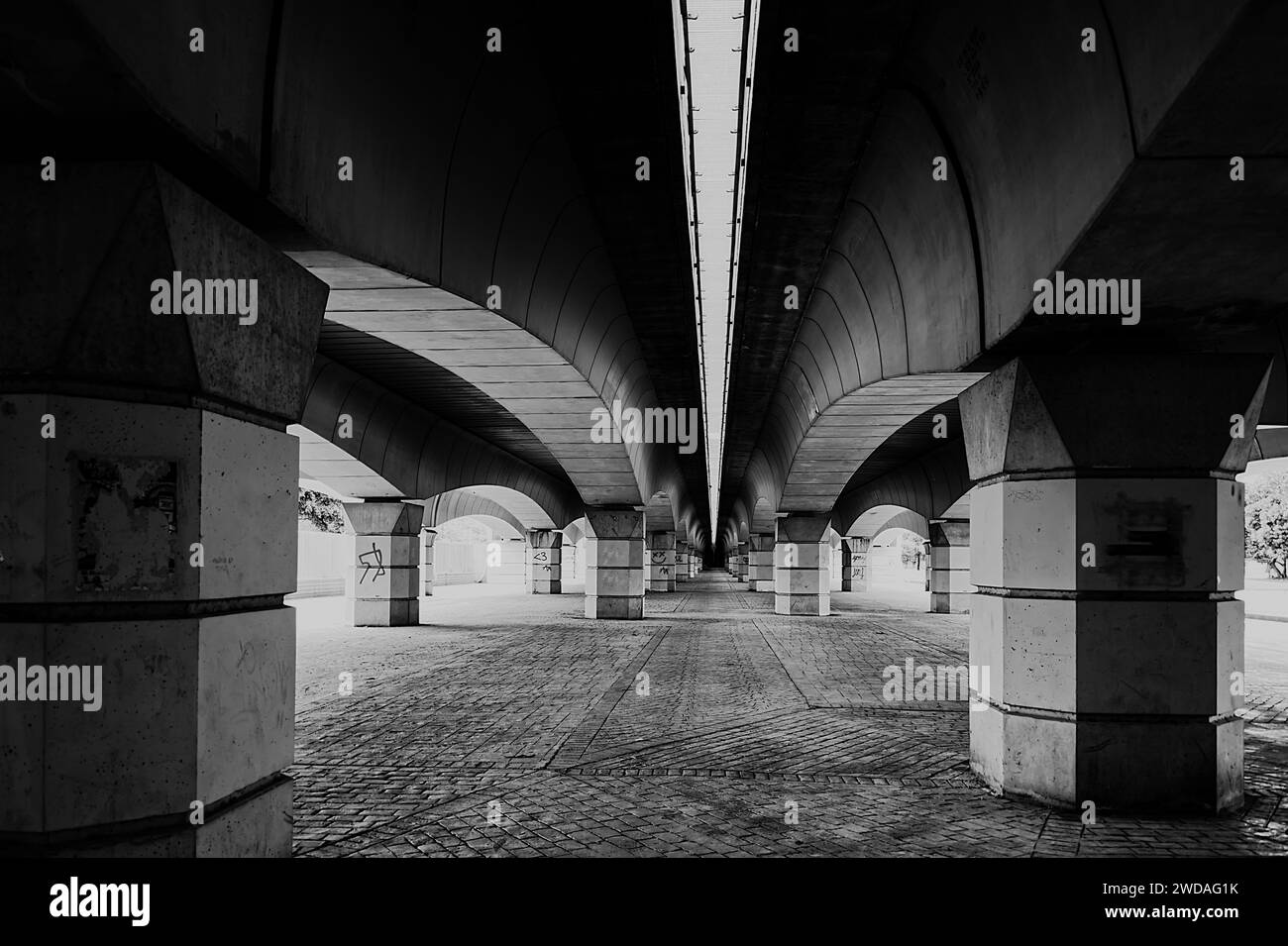 Area pedonale sotto la solida costruzione del ponte in bianco e nero Foto Stock
