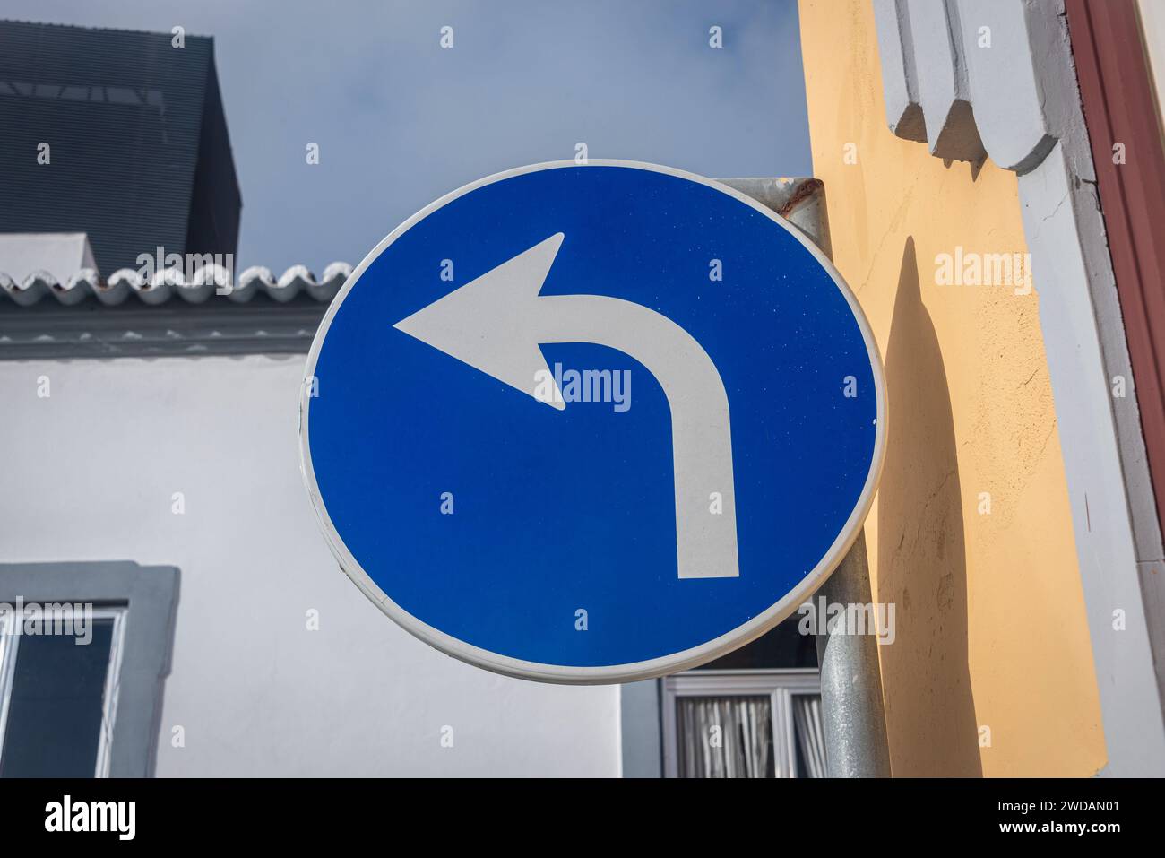Svolta a sinistra, cerchio blu con freccia bianca sul lato di un edificio Foto Stock