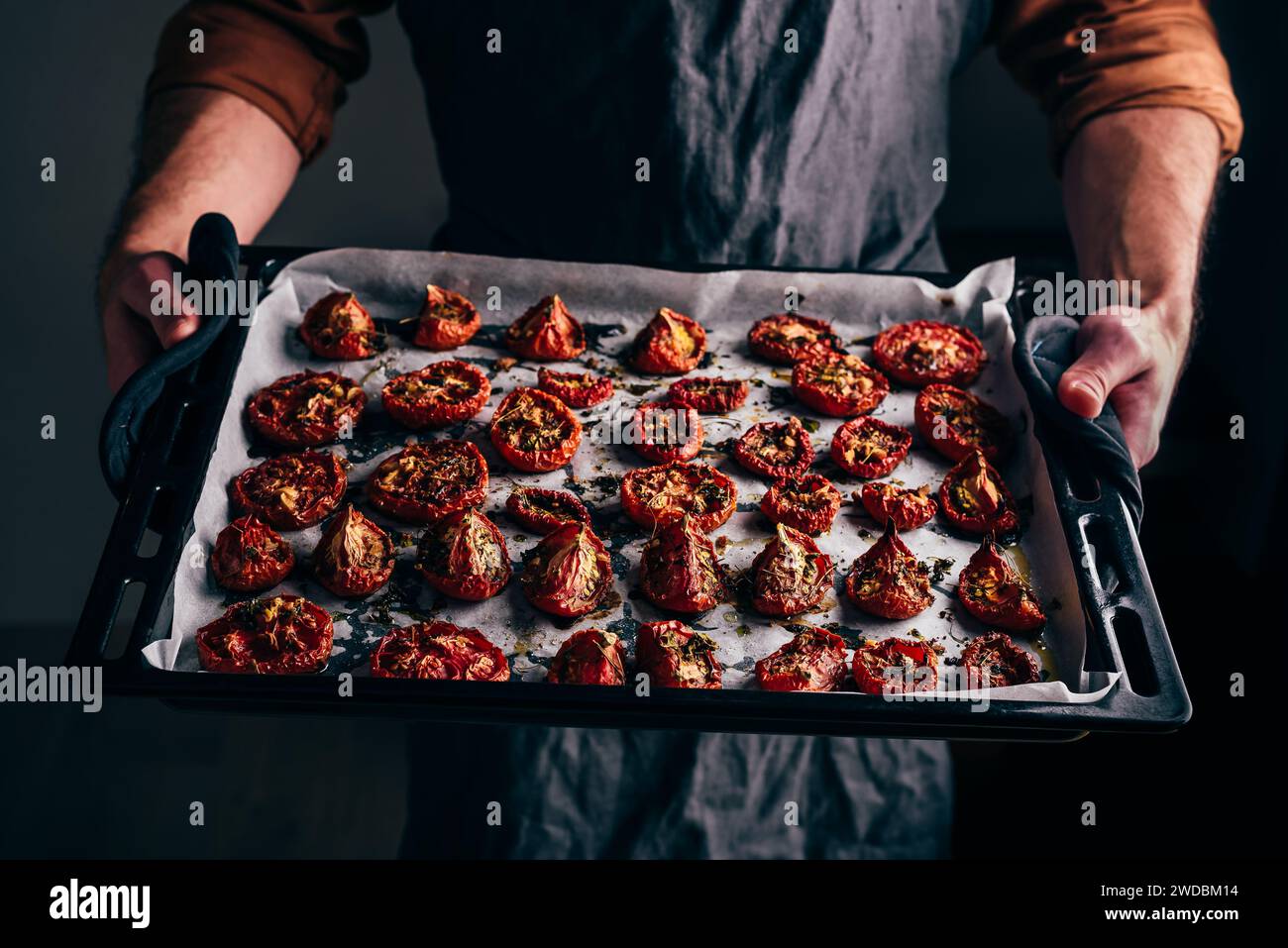 Teglia da forno con pomodori secchi appena preparati con olio d'oliva e timo in mani maschili Foto Stock