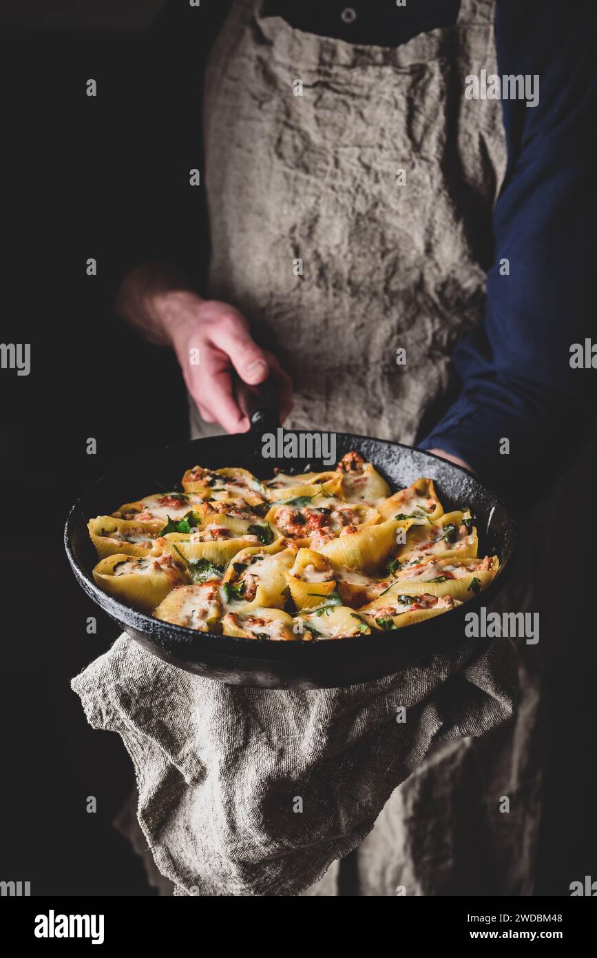 Lo chef conserva la padella di conchiglie di jumbo al forno ripieni di manzo macinato, spinaci e formaggio Foto Stock