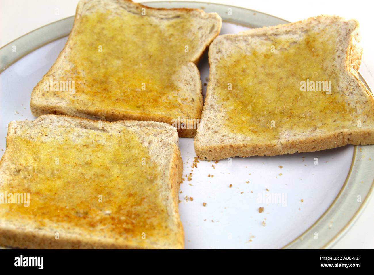Una foto di pezzi di pane tostato con burro su un piatto bianco su una scrivania. Foto Stock