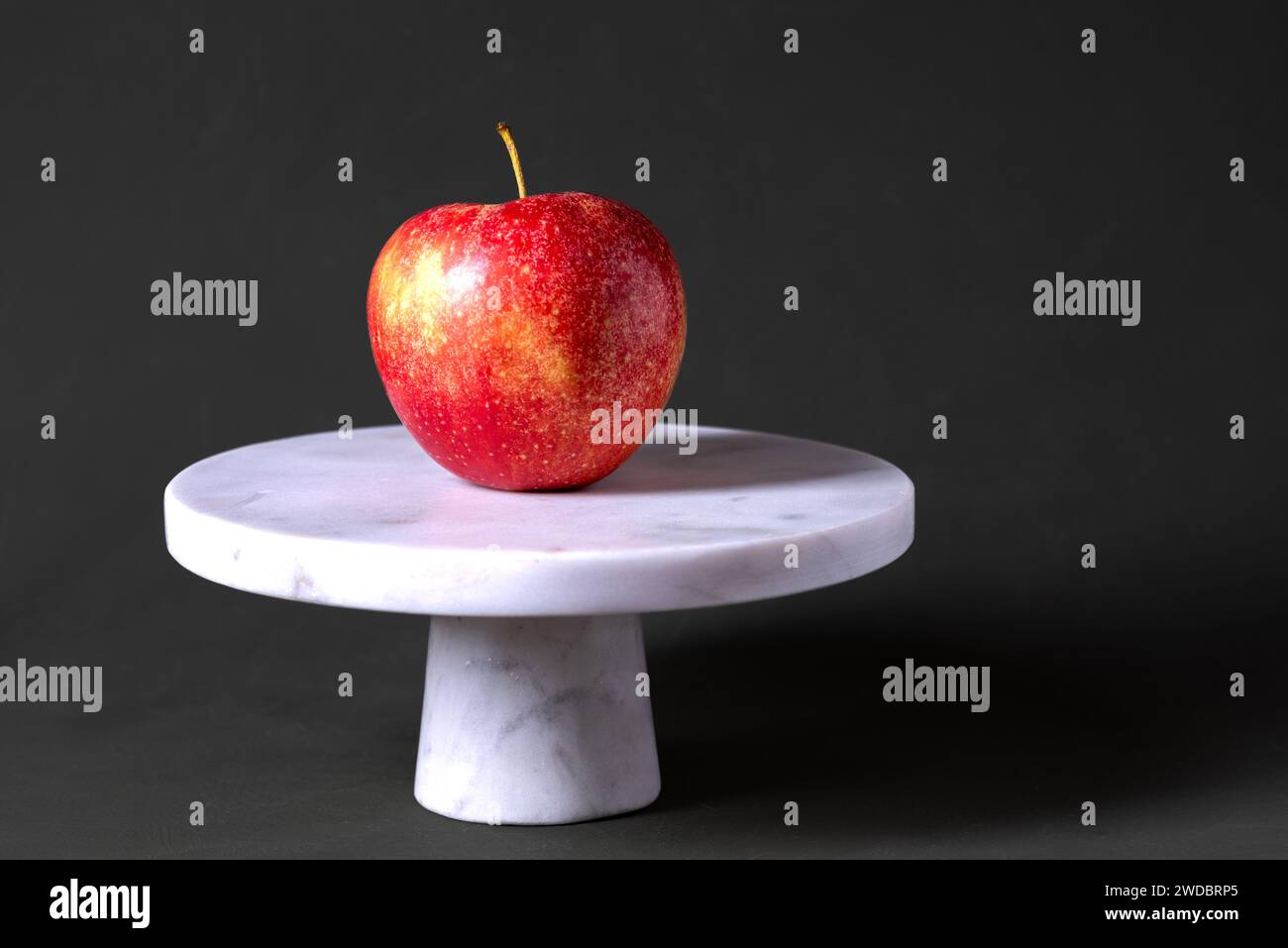 Un frutto di mela rossa su un supporto per torta con pietra bianca. Frutta. Foto Stock