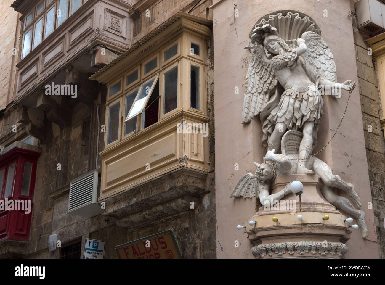 San Michele Arcangelo che uccide il diavolo che si trova ai suoi piedi. Statua fregio su edifici con balconi coperti a la Valletta, Malta, HOMER SYKES anni '2024 2020 Foto Stock