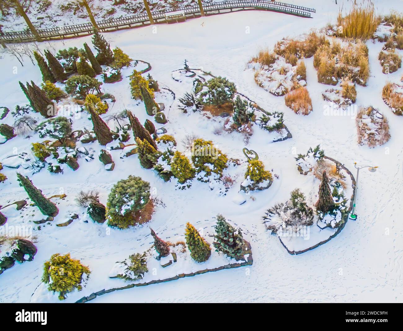 Vista aerea del parco pubblico innevato. Alberi sempreverdi e impronte di piedi nella neve visti dall'alto. Passerella in legno ai margini del parco su un Foto Stock