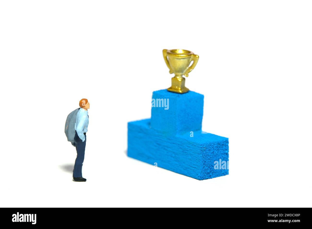 Fotografia di figure giocattolo in miniatura. Sognare di diventare un concetto da campione. Un uomo d'affari in piedi davanti al podio con trofeo d'oro. Isolare Foto Stock