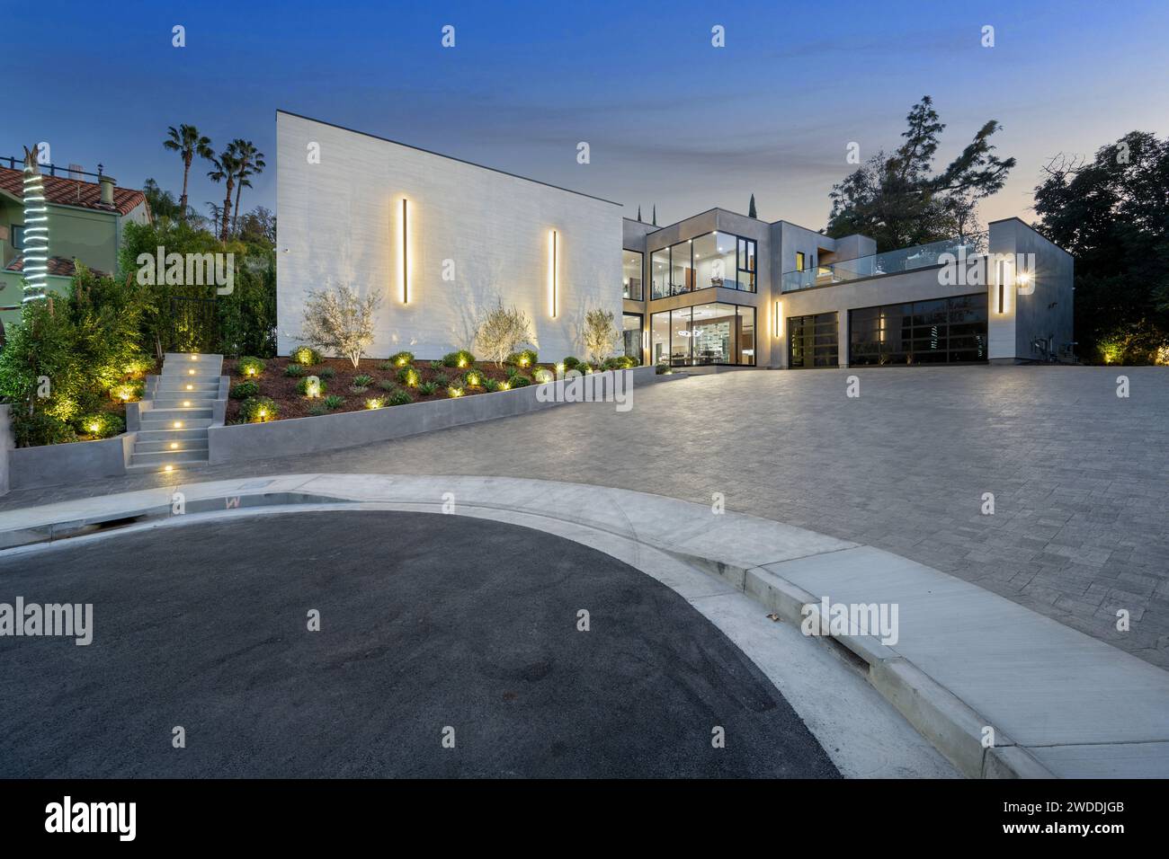 Una lussuosa villa in stucco e cemento con eleganti luci del cortile e un grande vialetto di ingresso, nuova casa di costruzione a Tarzana, California Foto Stock